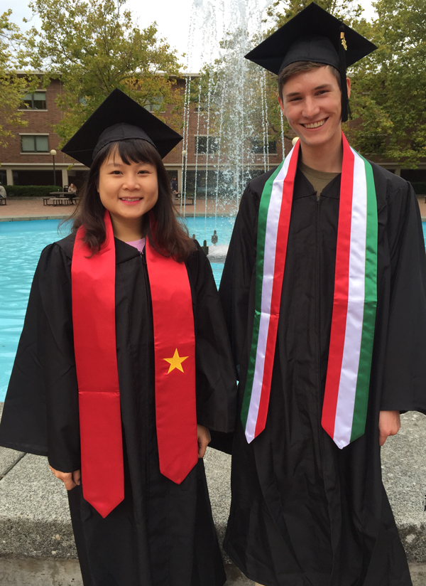 Two graduating students standing with the sashes made to match the flags of the countries in which they studied