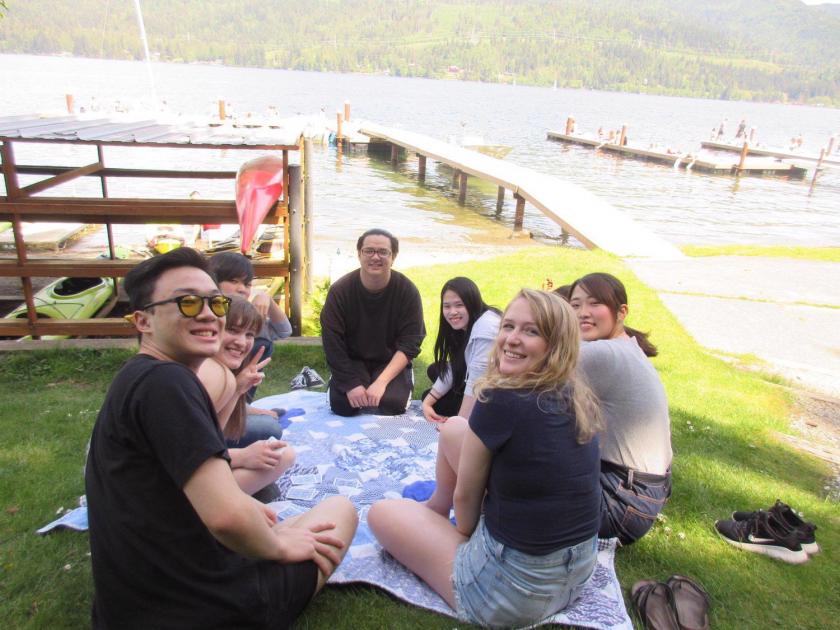 International Buddies (group of 8 students) at a picnic at Lakewood, sitting on the ground on a blue and white blanket, smiling at the camera.