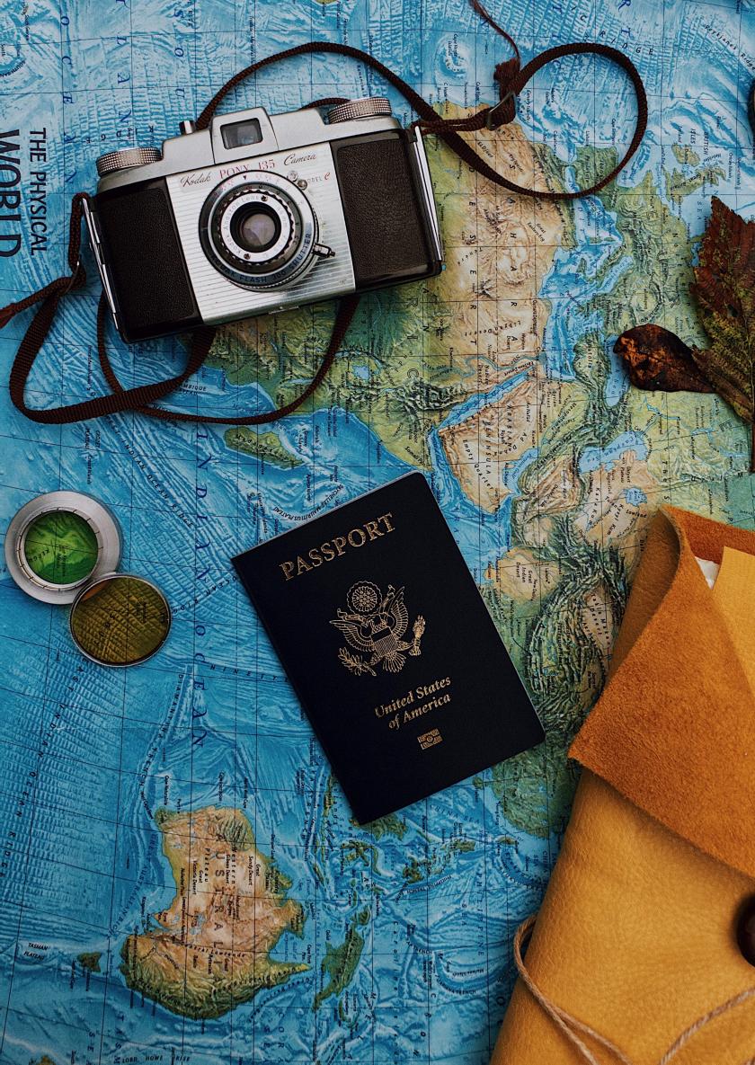 US Passport on a world map next to a camera, compass, and notebook.