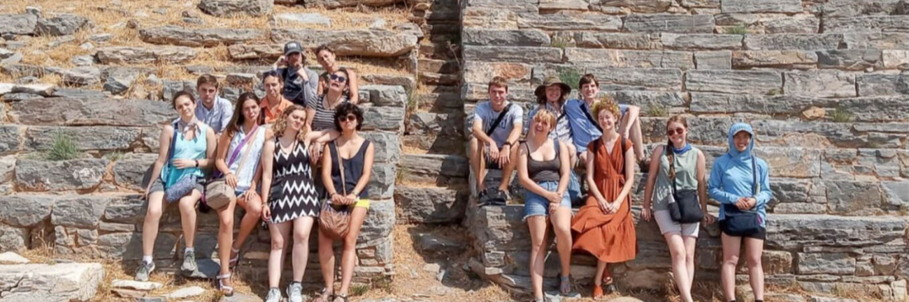 A group of Honors students sit on ancient ruins in Greece.