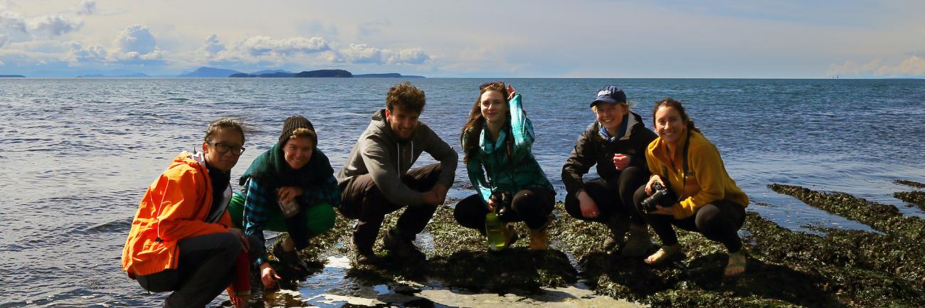 Six students crouching down near the Salish Sea